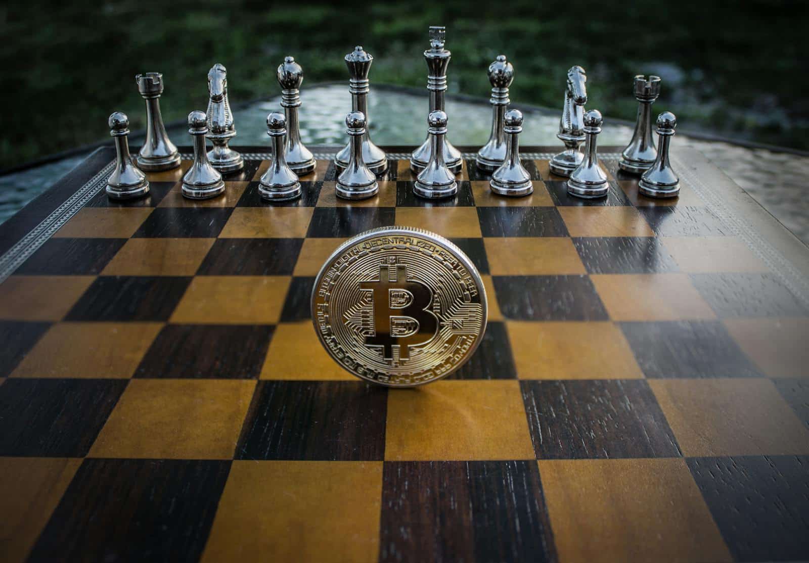 Bitcoin coin standing on a chessboard with silver and brass chess pieces. Concept of strategic digital currency investment.